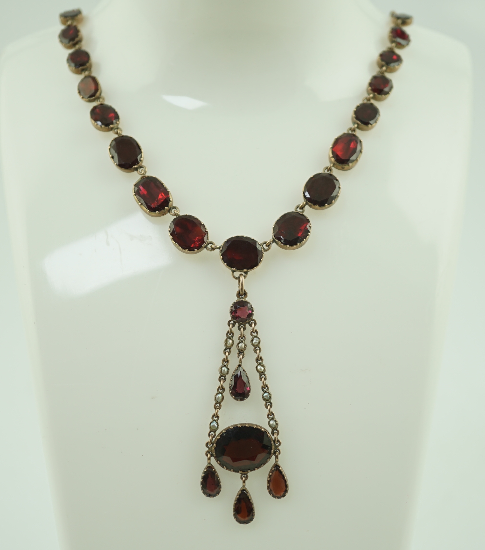 An early 19th century gold, and thirty five graduated foil backed garnet set necklace, with later garnet and seed pearl set drop